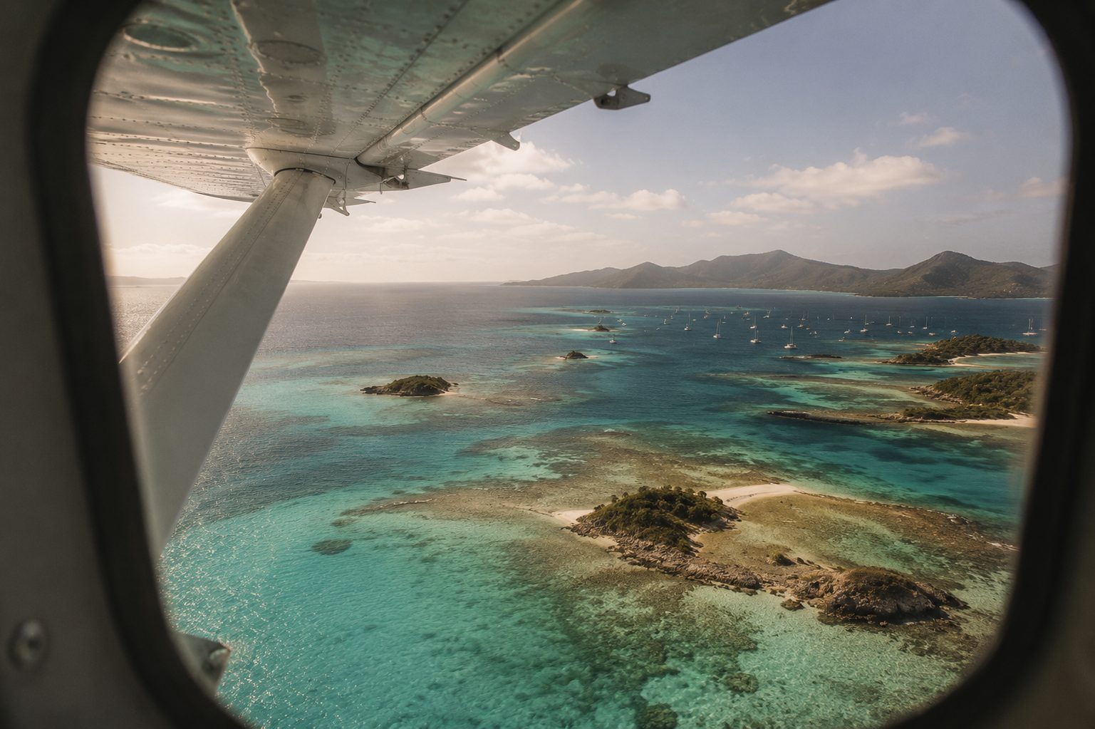 View from a small aircraft window over turquoise reefs and islands of the Grenadines